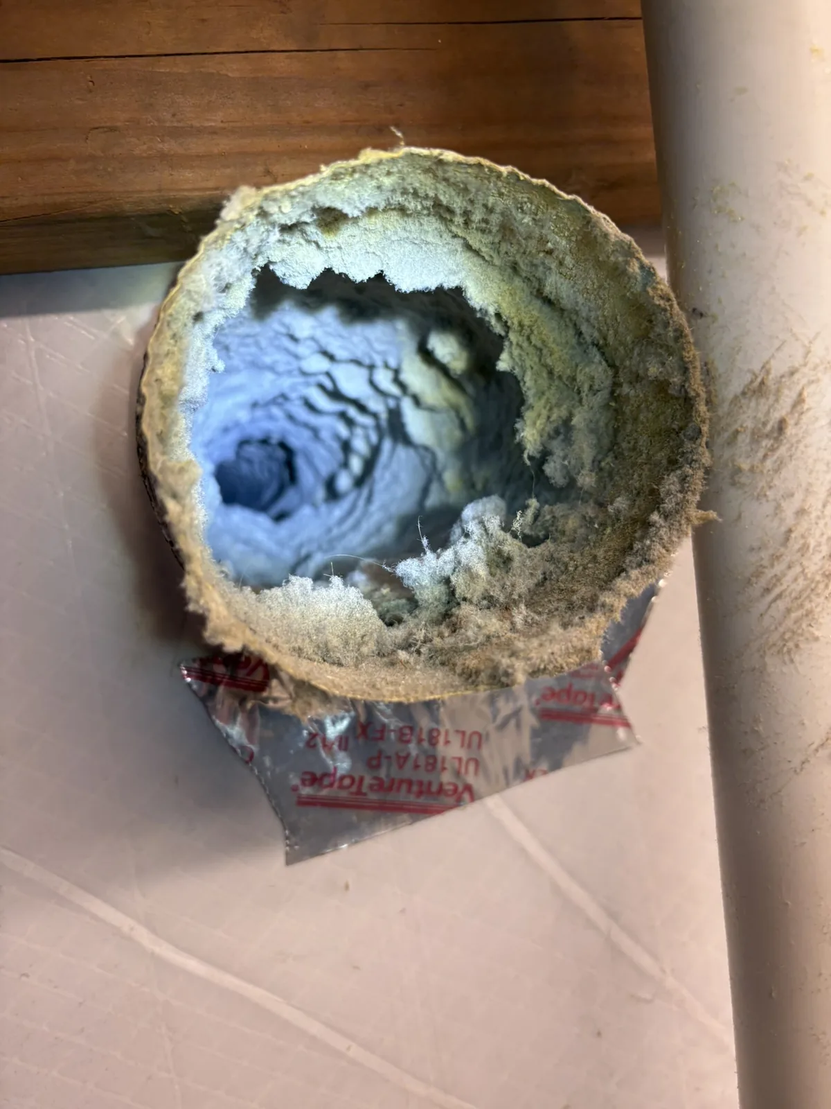 The lint-caked opening of a dryer vent duct where it exits into the laundry room