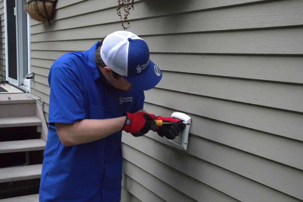 A Lint Guys technician working at an exterior dryer vent hood