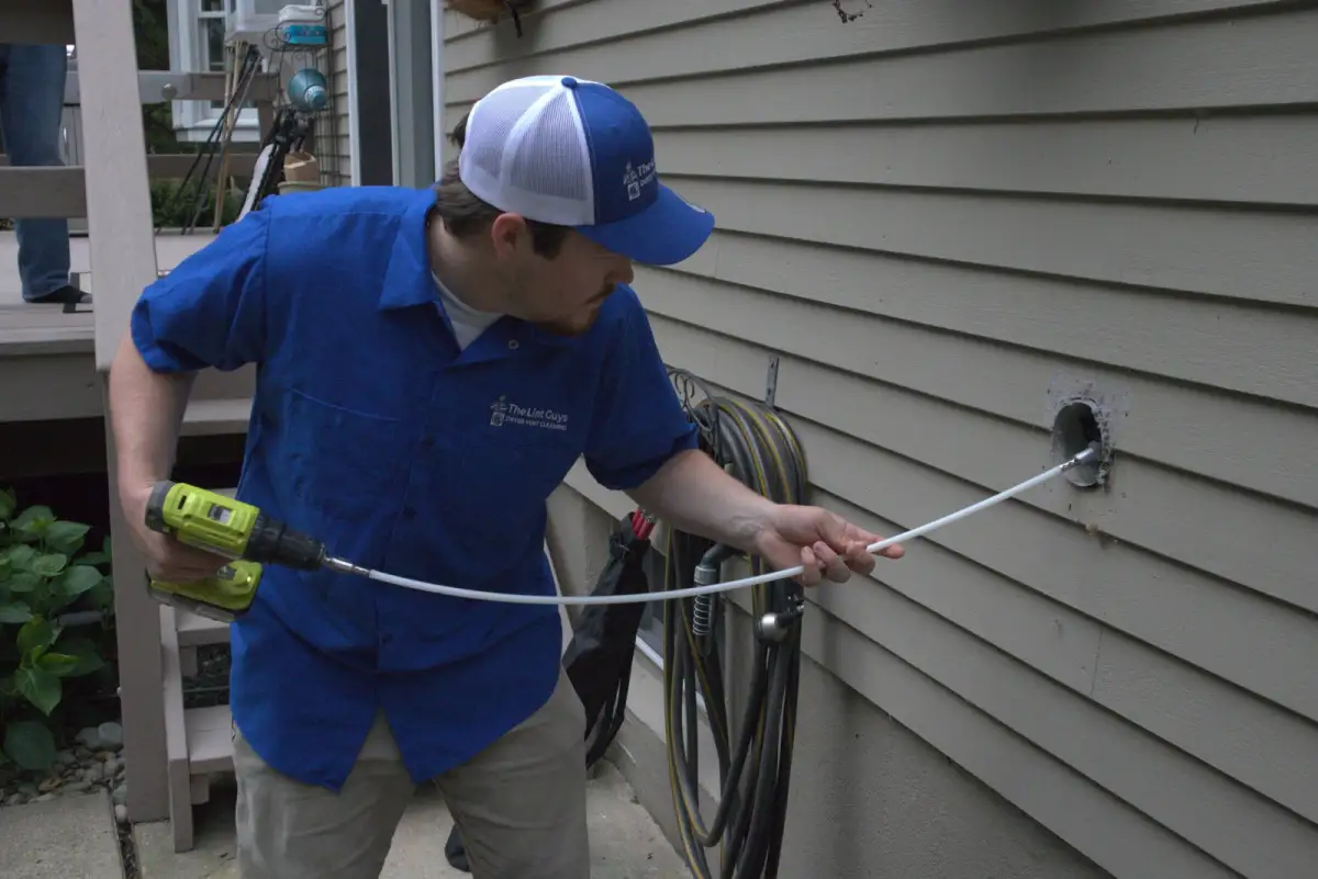 A Lint Guys technician feeding a cleaning line into an exterior dryer vent