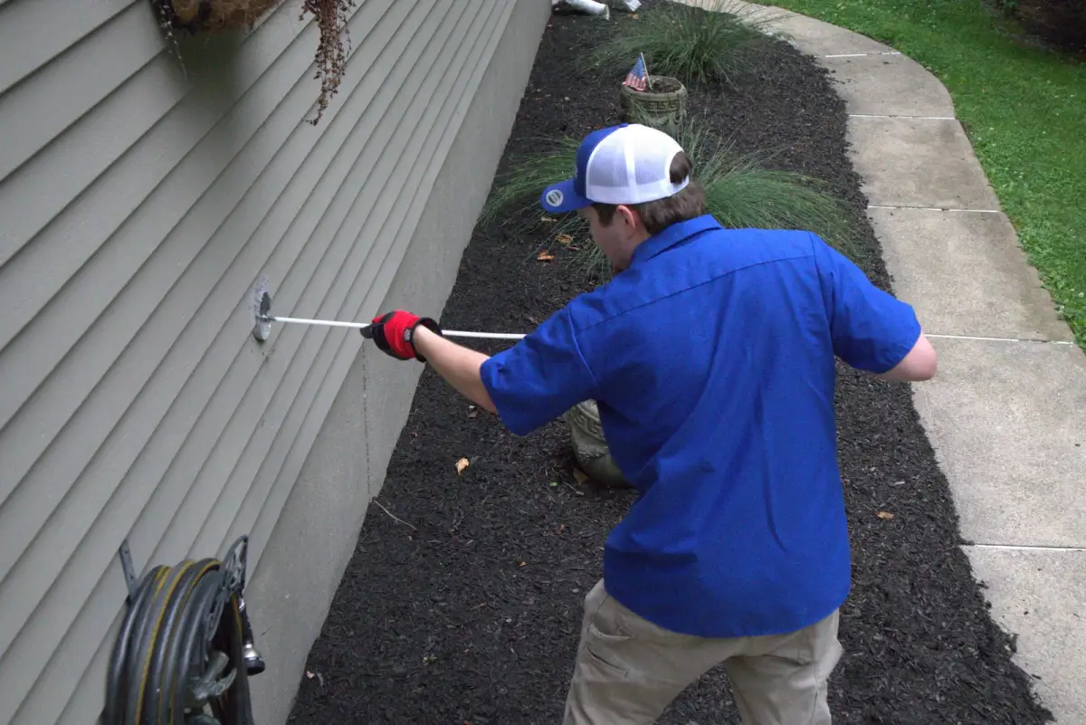 A Lint Guys technician clearing a dryer vent line from outside the house