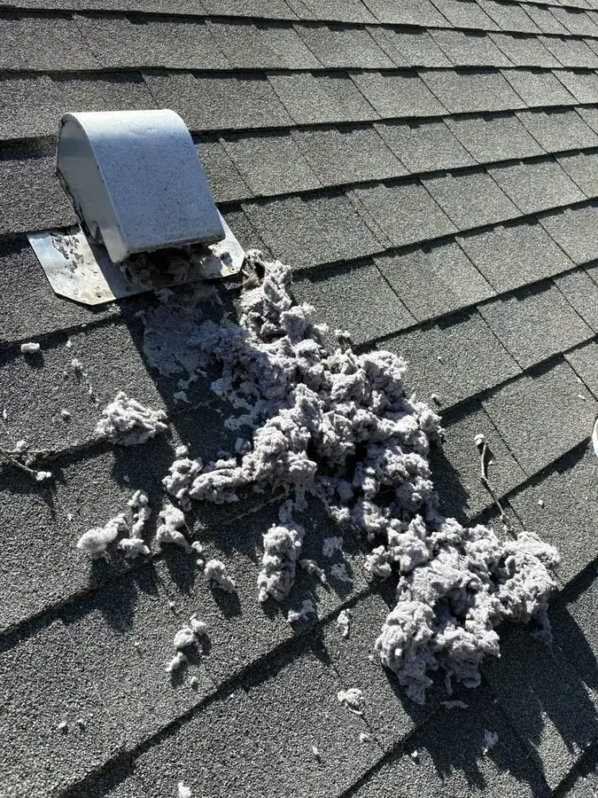 A heap of grey dryer lint spilling from a hooded metal roof vent