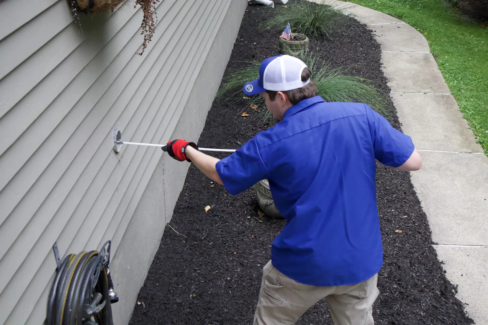 A Lint Guys technician cleaning an exterior dryer vent on the side of a house with a rotary line