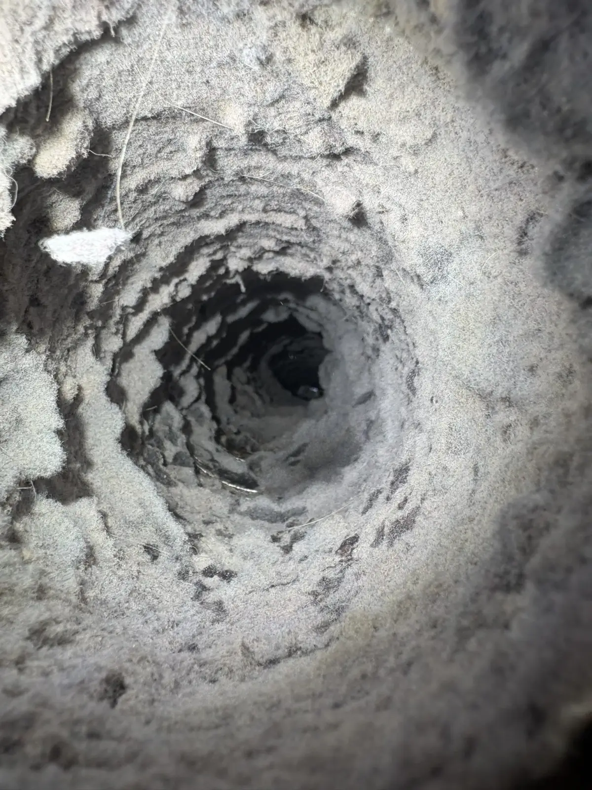 The inside of a dryer vent duct packed with thick lint, leaving only a narrow opening