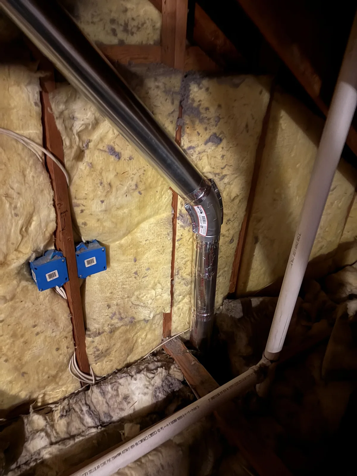 A rigid metal dryer duct run through an attic between insulated framing