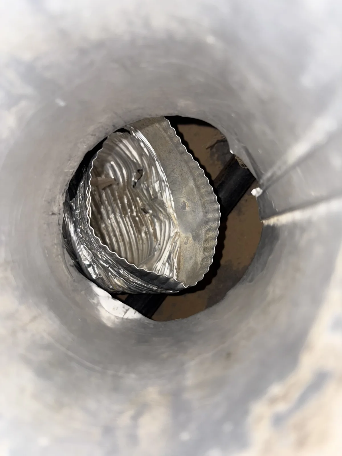 Looking down a metal dryer duct at a crushed foil connector inside