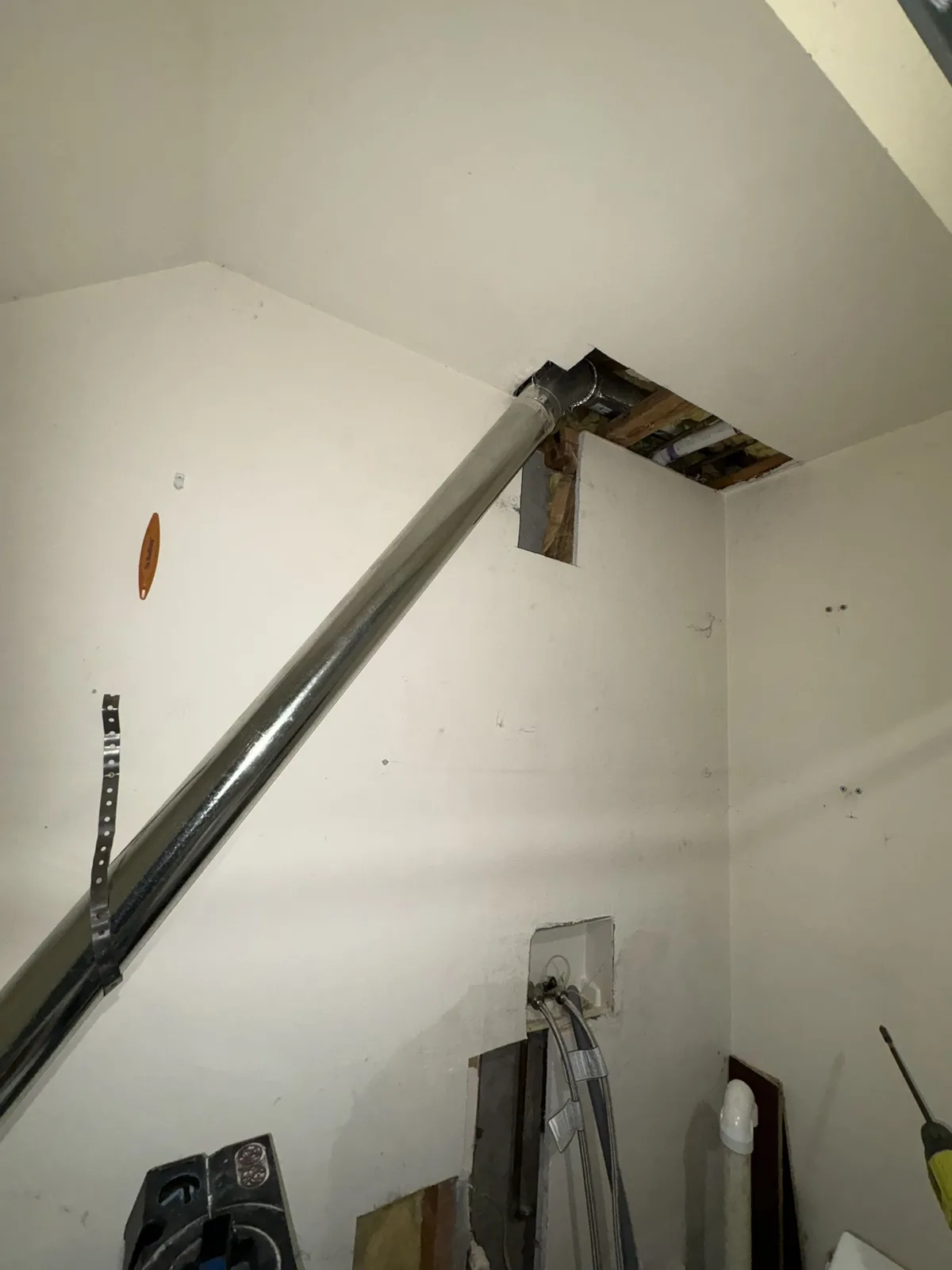 A rigid metal dryer duct angled up a laundry room wall to an opening in the ceiling
