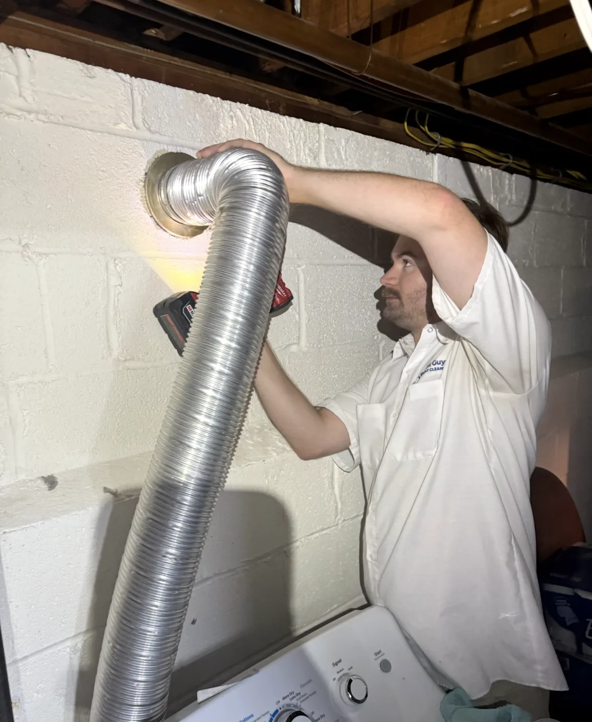 A technician holding flexible foil duct to a round opening in a white block wall