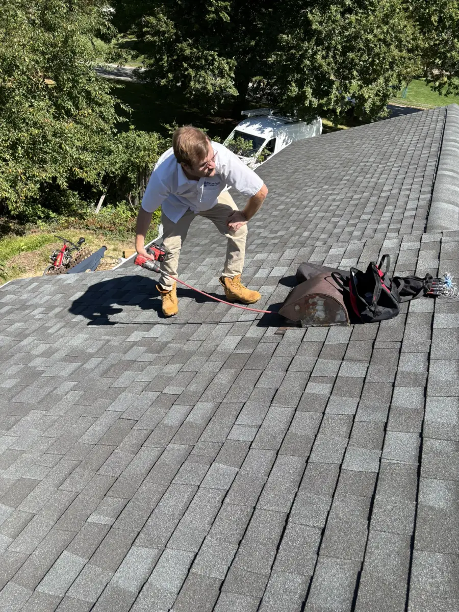 A technician on a roof running a red cleaning line into a rusted vent