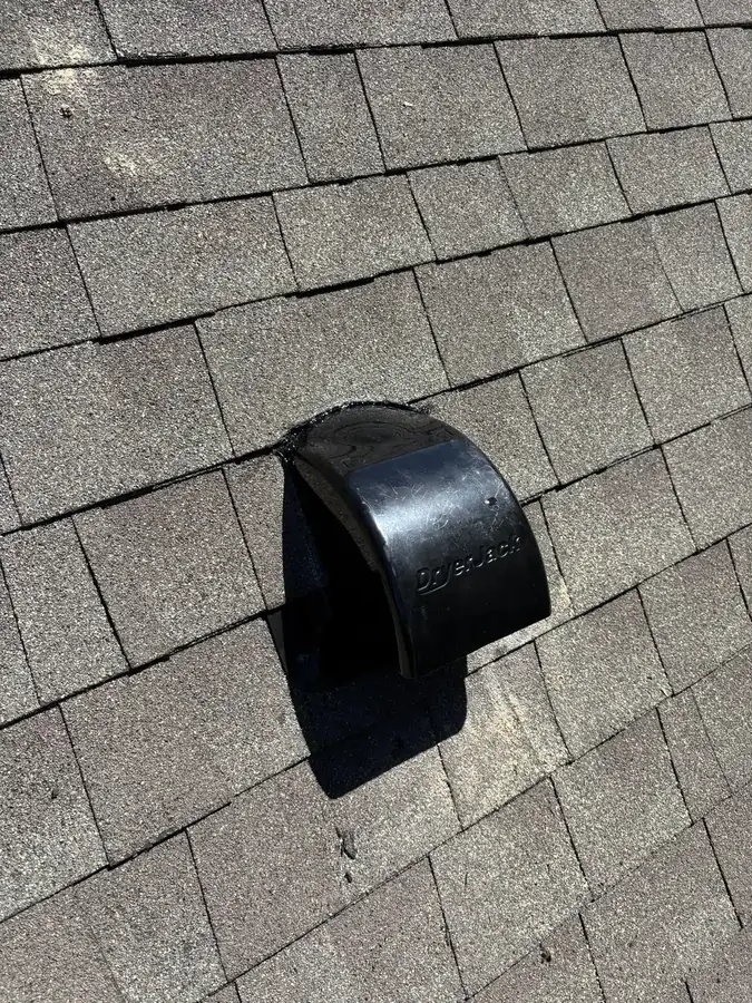 A black low-profile roof dryer vent installed on an asphalt shingle roof