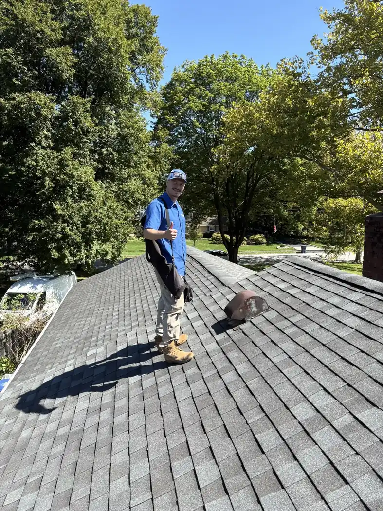A Lint Guys technician working on a dryer vent on an asphalt shingle roof