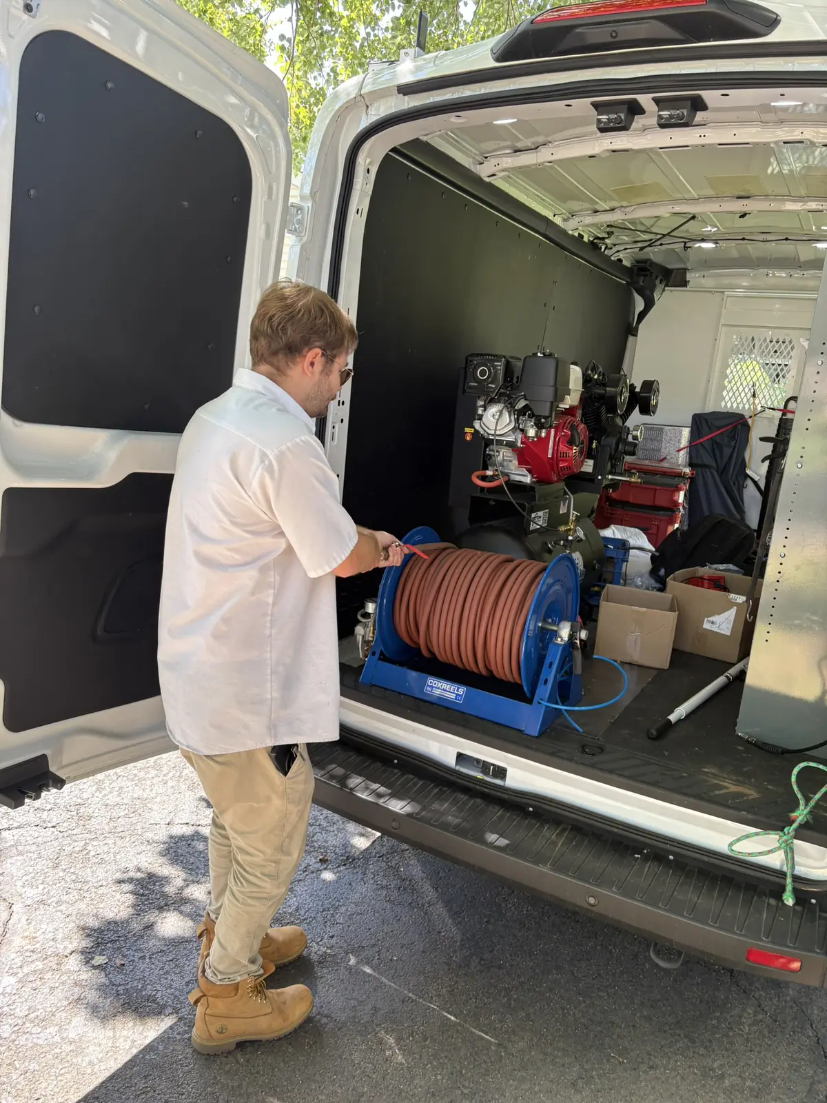 A technician at the open rear doors of the service van with the cleaning equipment