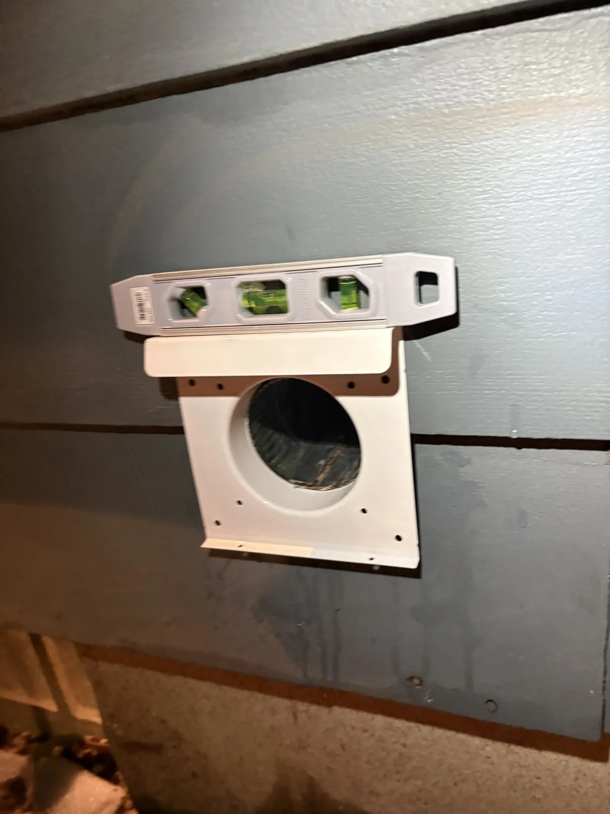 A new low-profile dryer wall hood being fitted over the wall penetration